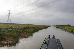 Heading towards Welney on the Old Bedford river in November 2016. NB Olive Emily is about to run into a mass of cott weed and an undredged length of the river that runs beneath the power cables three miles from Salters Lode. This is evident from the uncovered section of bank underneath the pylons and the continuation of dredging further along towards Welney and Welched Dam lock.